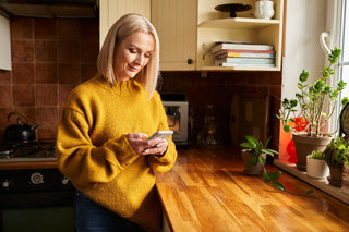Woman in cozy sweater scrolling her phone in the kitchen—exploring hormone health and menopause advice online